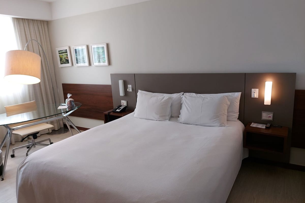A hotel room with a large bed, a desk with a chair, a lamp, and a nightstand with a phone.