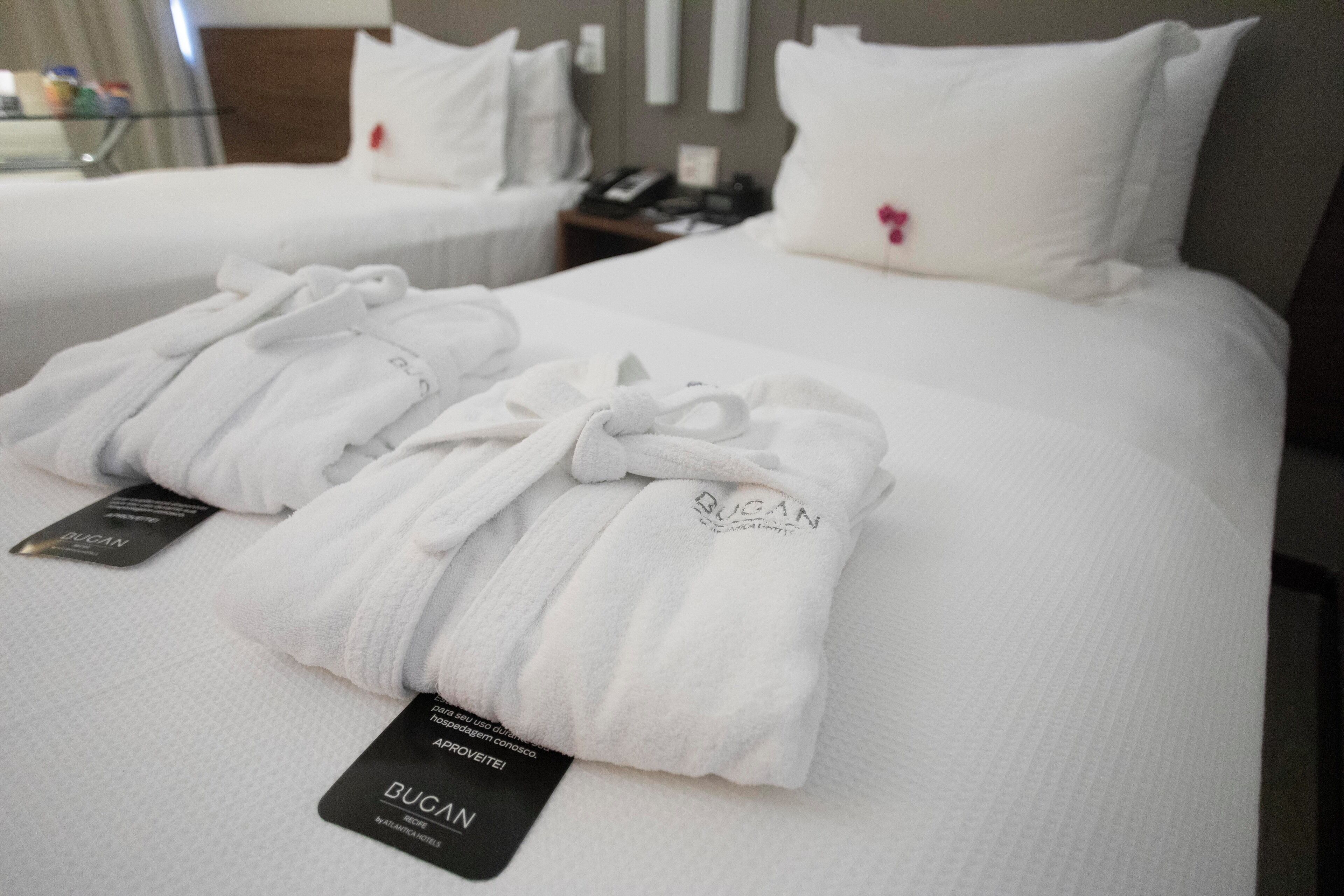 Two neatly made beds with white bedding and pillows, each with a tag labeled "BUCAN."