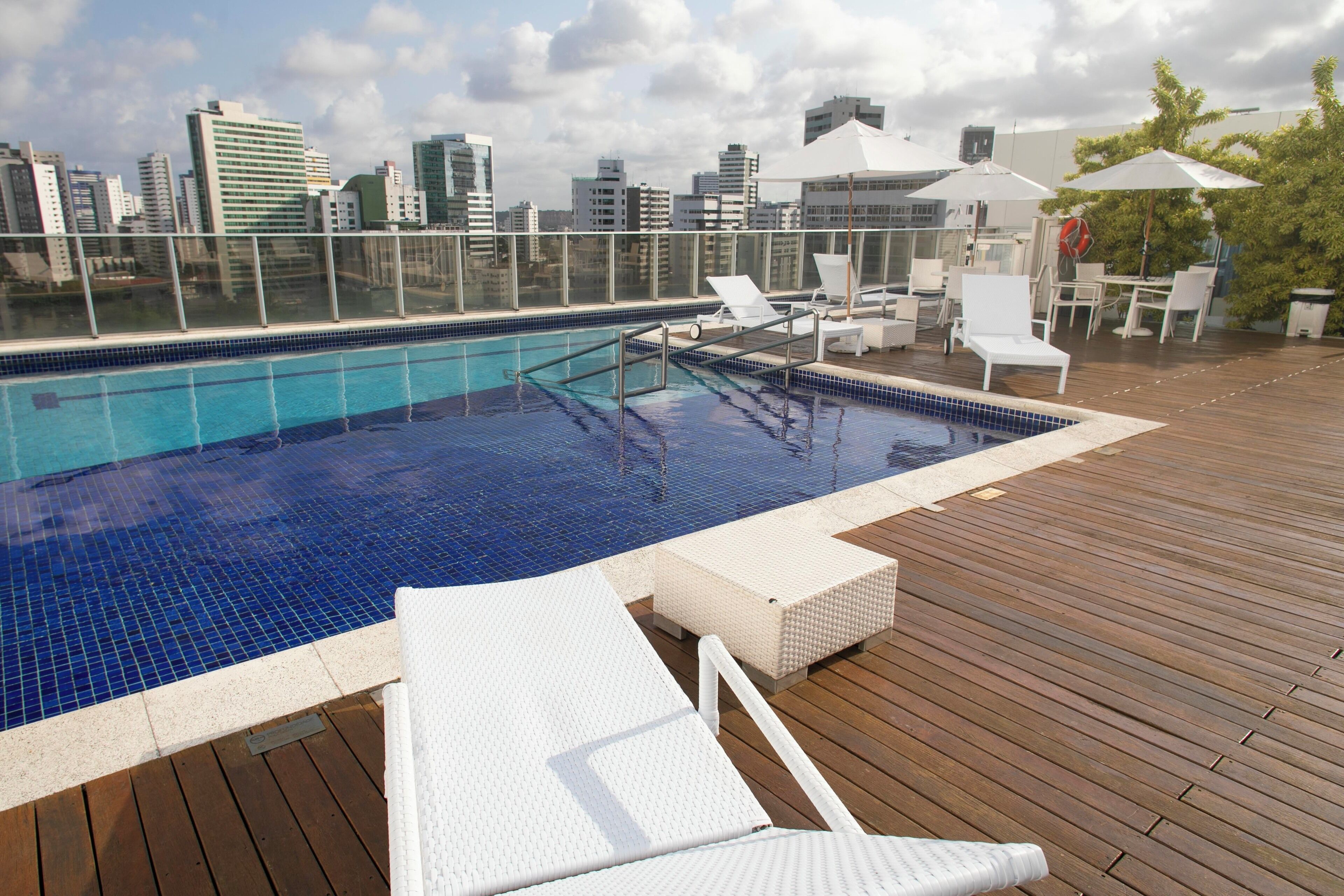 A rooftop pool with a city skyline view, white lounge chairs, and umbrellas.