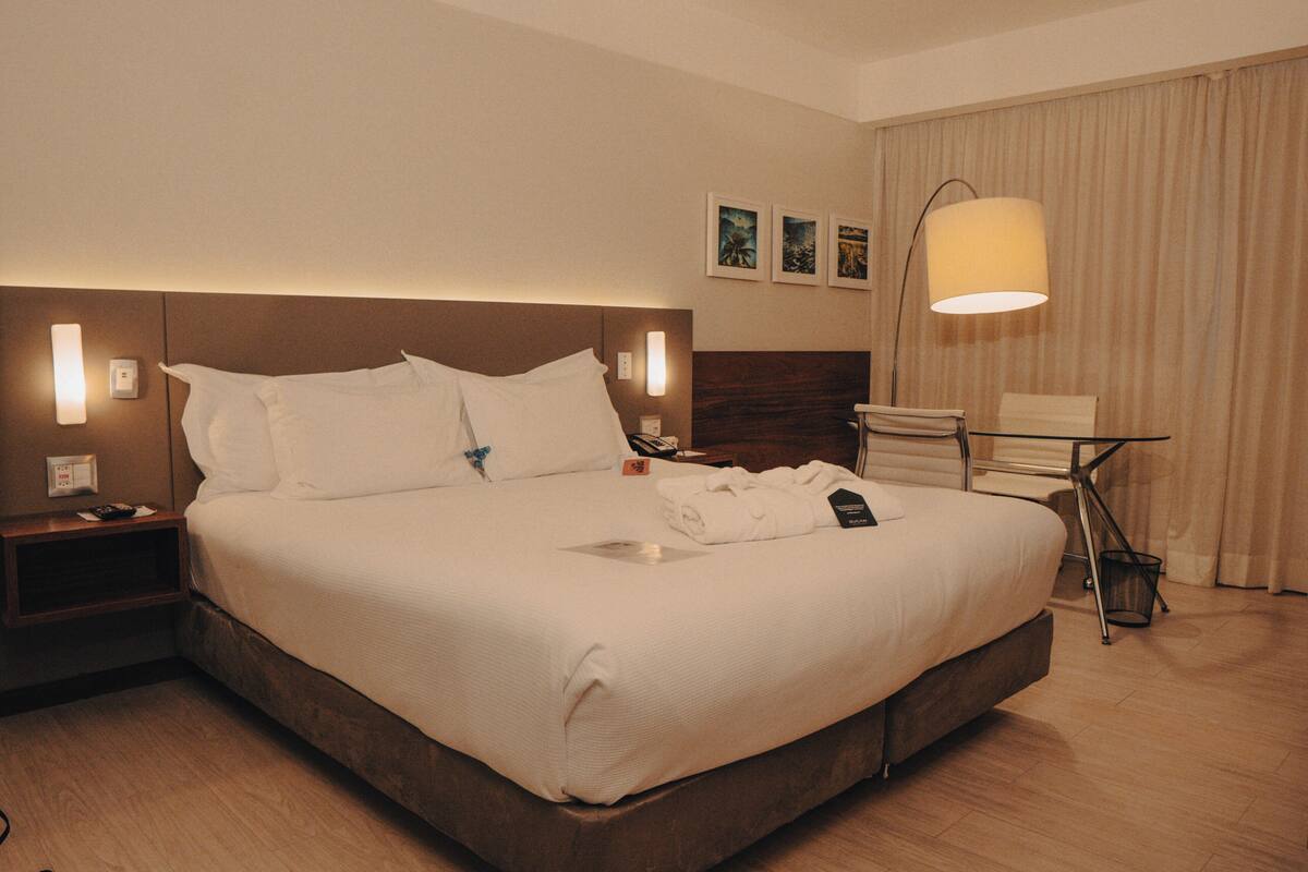 A hotel room with a large bed, bedside tables, a desk, a chair, and a lamp.
