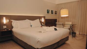 A hotel room with a large bed, bedside tables, a desk, a chair, and a lamp.