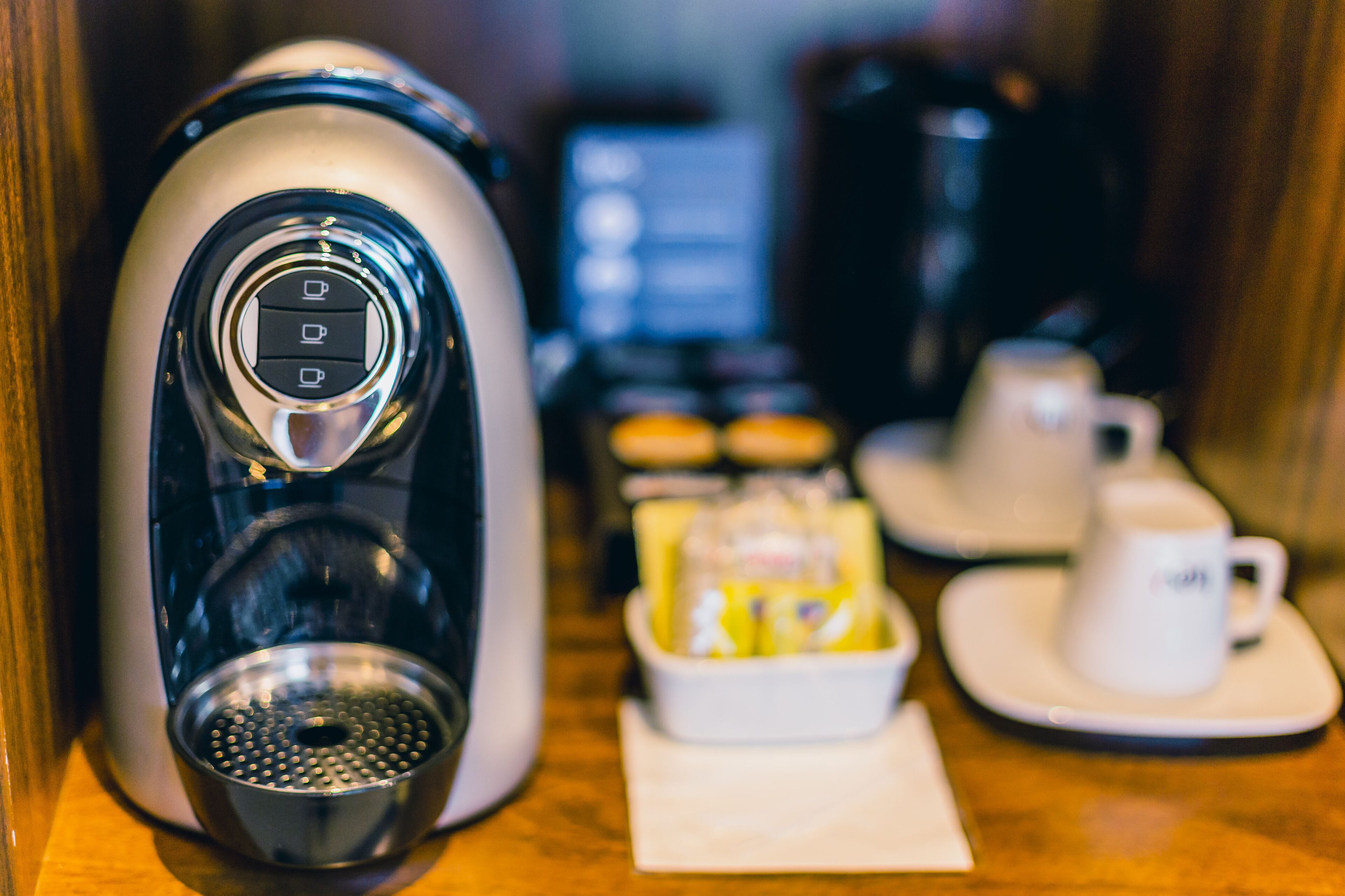 A coffee machine with a digital display, a coffee pot, a tray of pastries, and a cup and saucer on a wooden table.