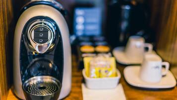 A coffee machine with a digital display, a coffee pot, a tray of pastries, and a cup and saucer on a wooden table.
