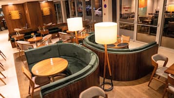 A modern interior with green cushioned seating, wooden tables, and lamps.