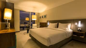 A hotel room with a large bed, bedside tables, a desk, and a view of the outside.