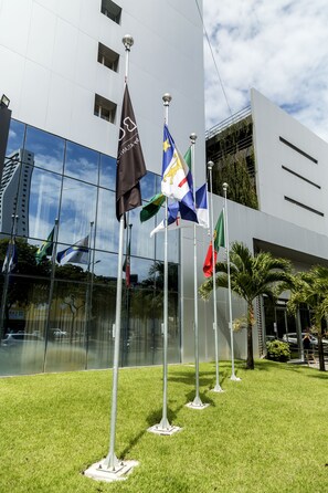 Un edificio moderno con varias banderas, incluyendo la bandera brasileña, frente a un fachada de vidrio.