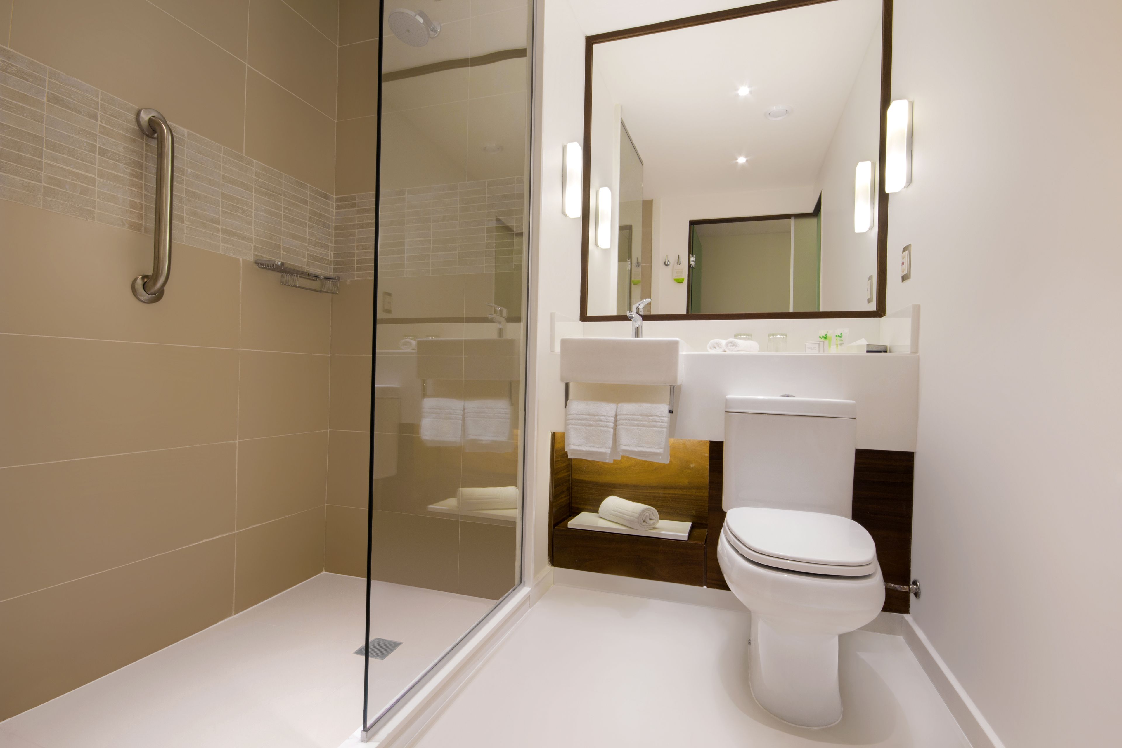 Un baño moderno con cabina de ducha de vidrio, un lavabo blanco y un espejo grande sobre el mueble.