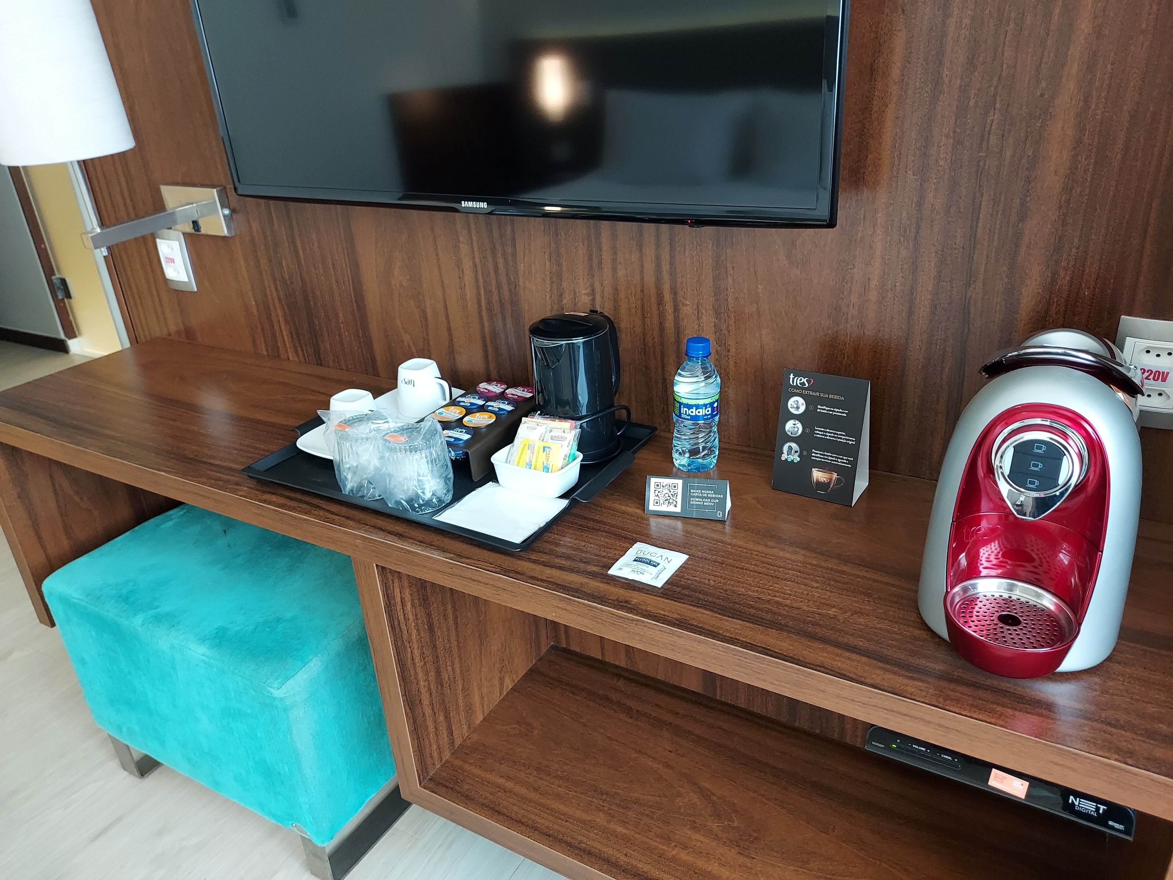 A hotel reception desk with a flat-screen TV, a coffee maker, a water bottle, and a sign with instructions.