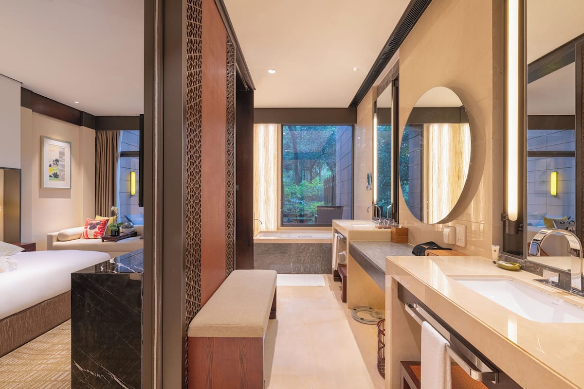 Une salle de bain d’hôtel moderne, dotée d’un grand miroir, de deux vasques, d’une baignoire et d’un banc.