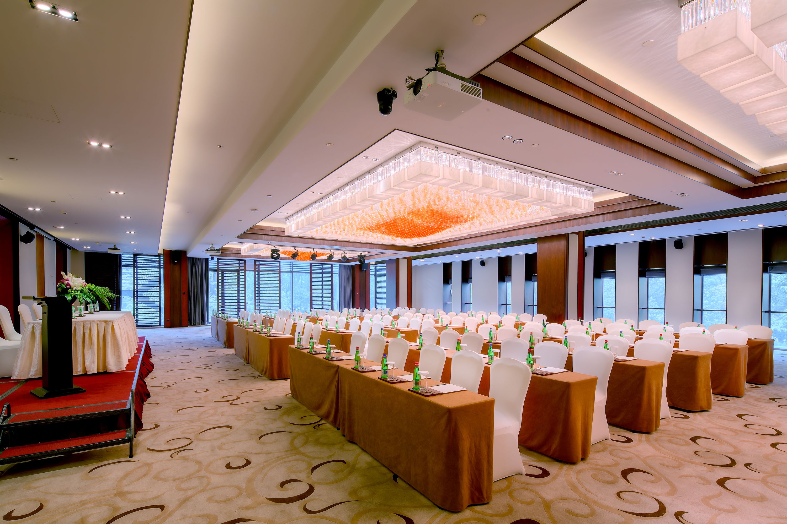 A conference room with rows of tables, white chairs, and a podium.