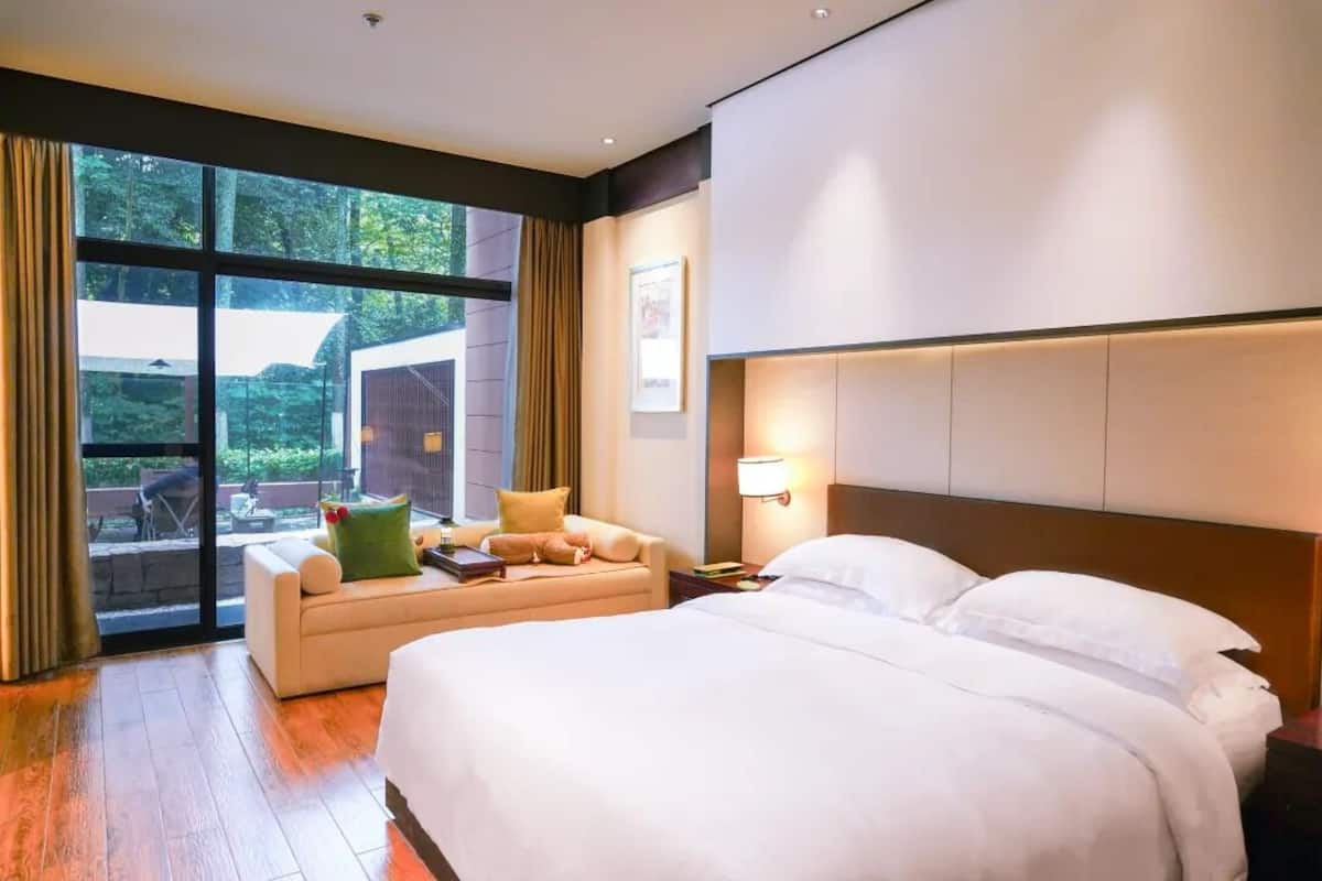 Une chambre d’hôtel avec un grand lit, un canapé, une table de chevet et une fenêtre avec des rideaux.