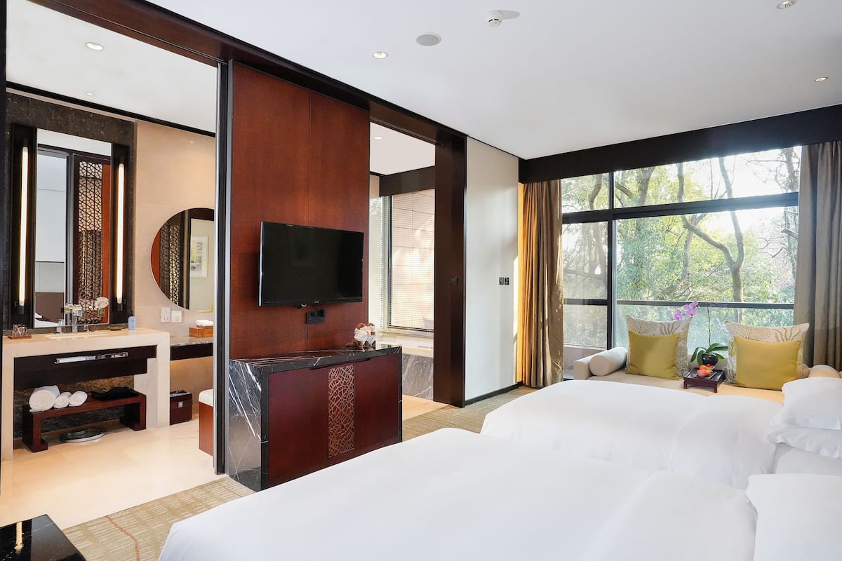 Une chambre d’hôtel moderne dotée d’un grand lit, d’une télévision, d’un bureau avec un ordinateur et d’une fenêtre donnant sur la verdure.