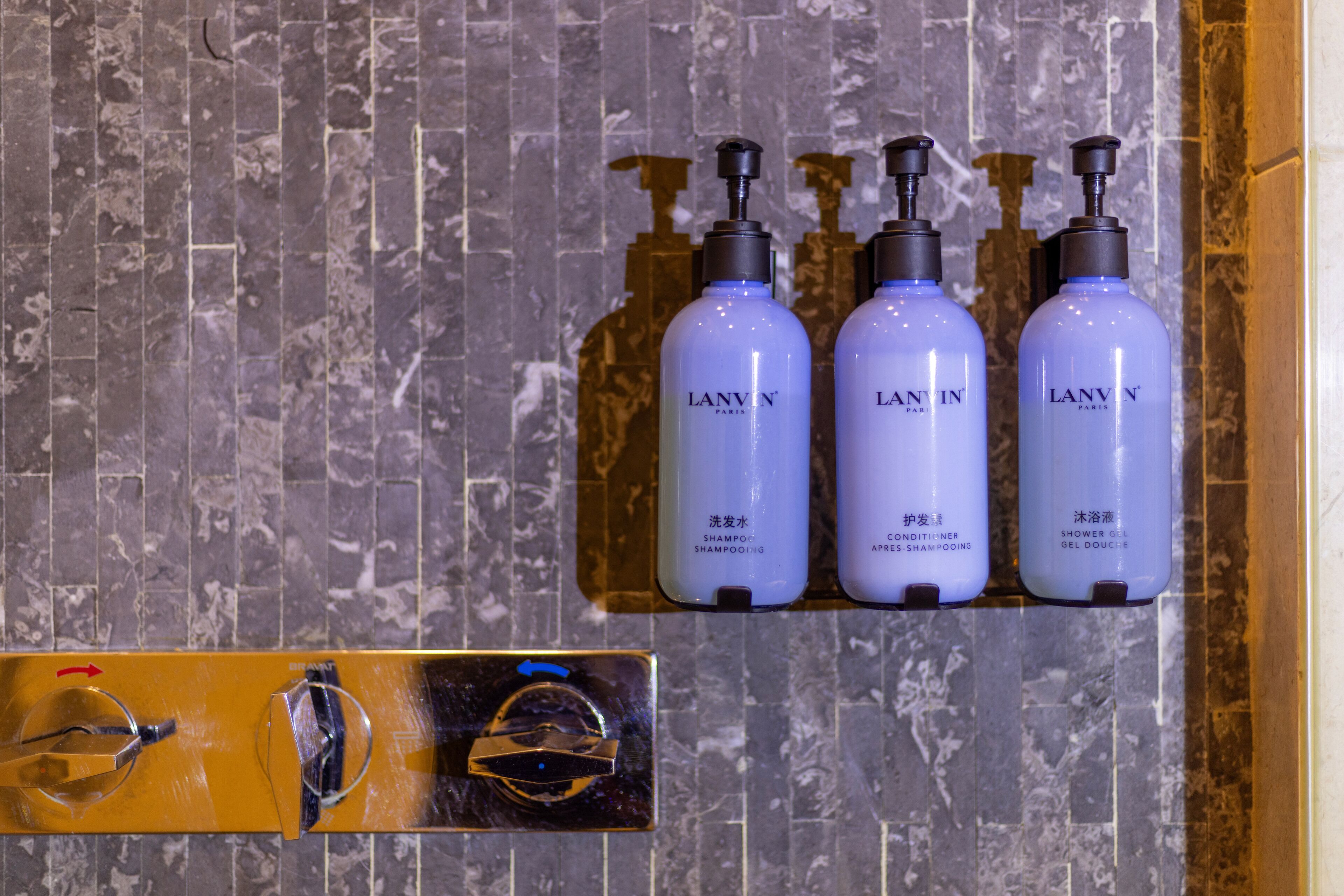 A bathroom with a marble wall and three Lanvin shampoo bottles.