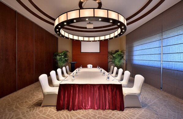 A conference room with a long table, white chairs, and a red tablecloth.