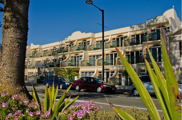 A multi-story hotel with balconies, a street in front, and tropical plants. - Beach Front Motel Napier (Napier)
