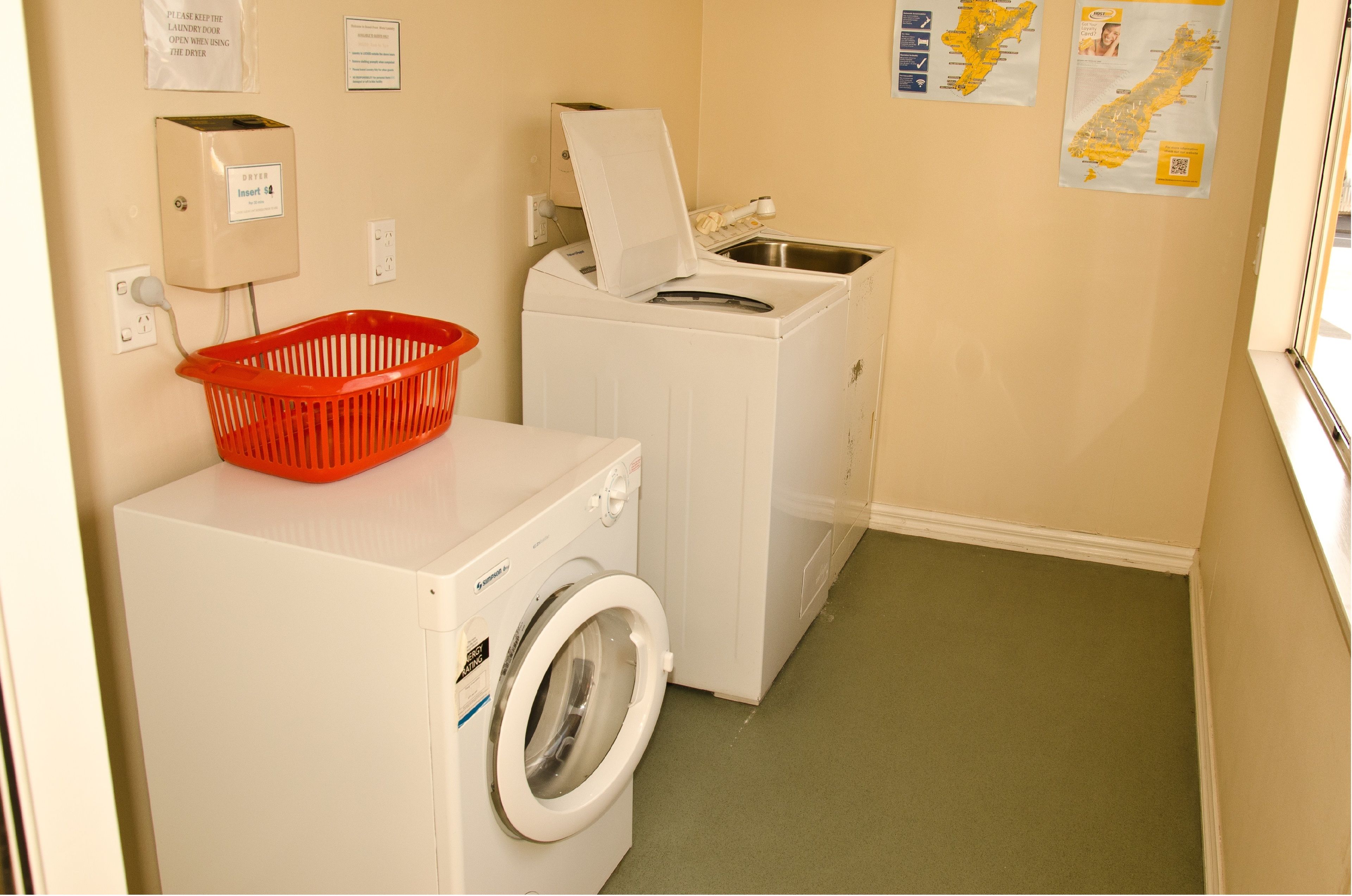 A laundry room with a front-loading washer and dryer, a red laundry basket, and a map on the wall.