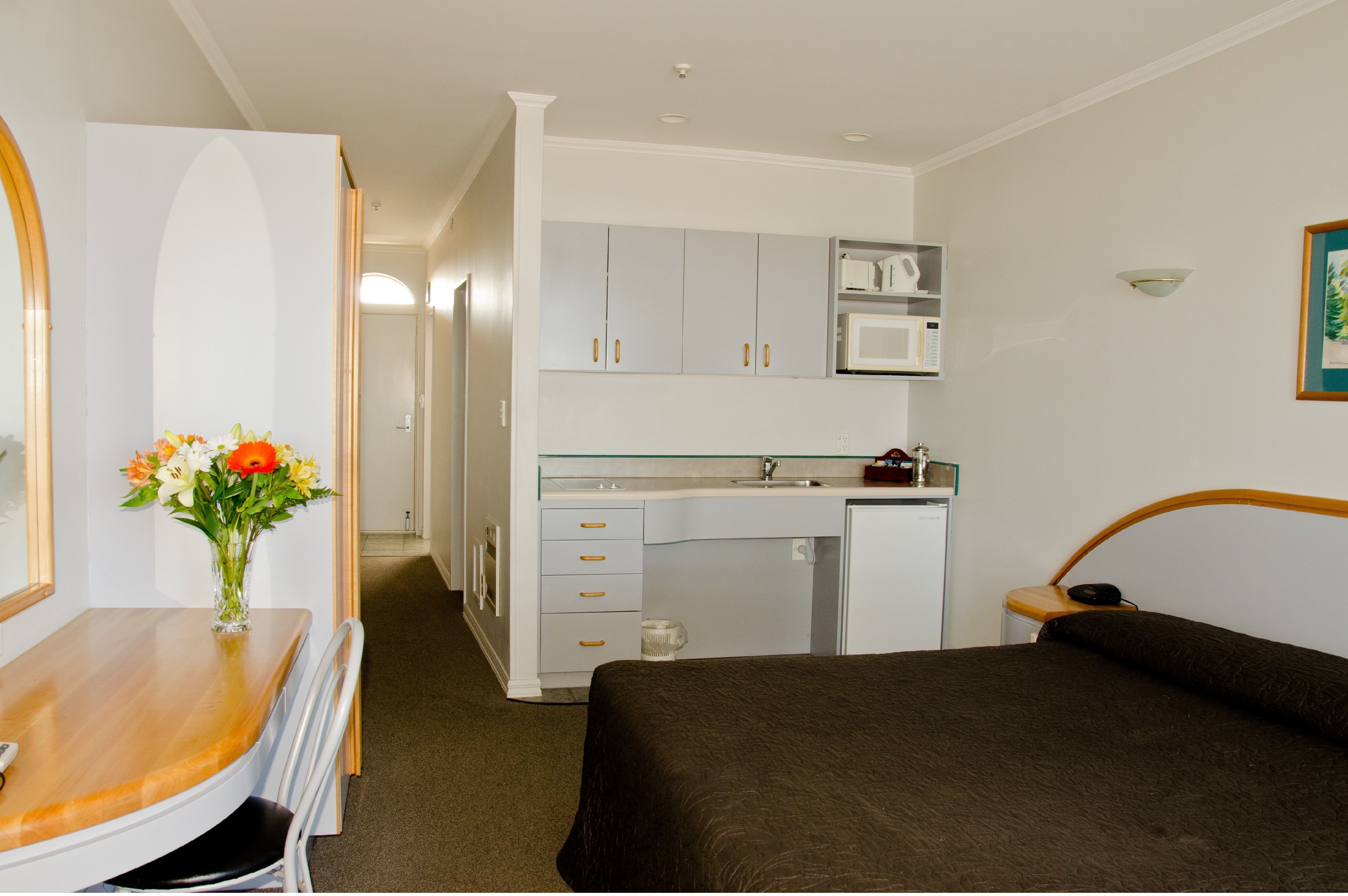 Une chambre d’hôtel comprenant un lit, un bureau avec une chaise, une petite kitchenette et une salle de bain.