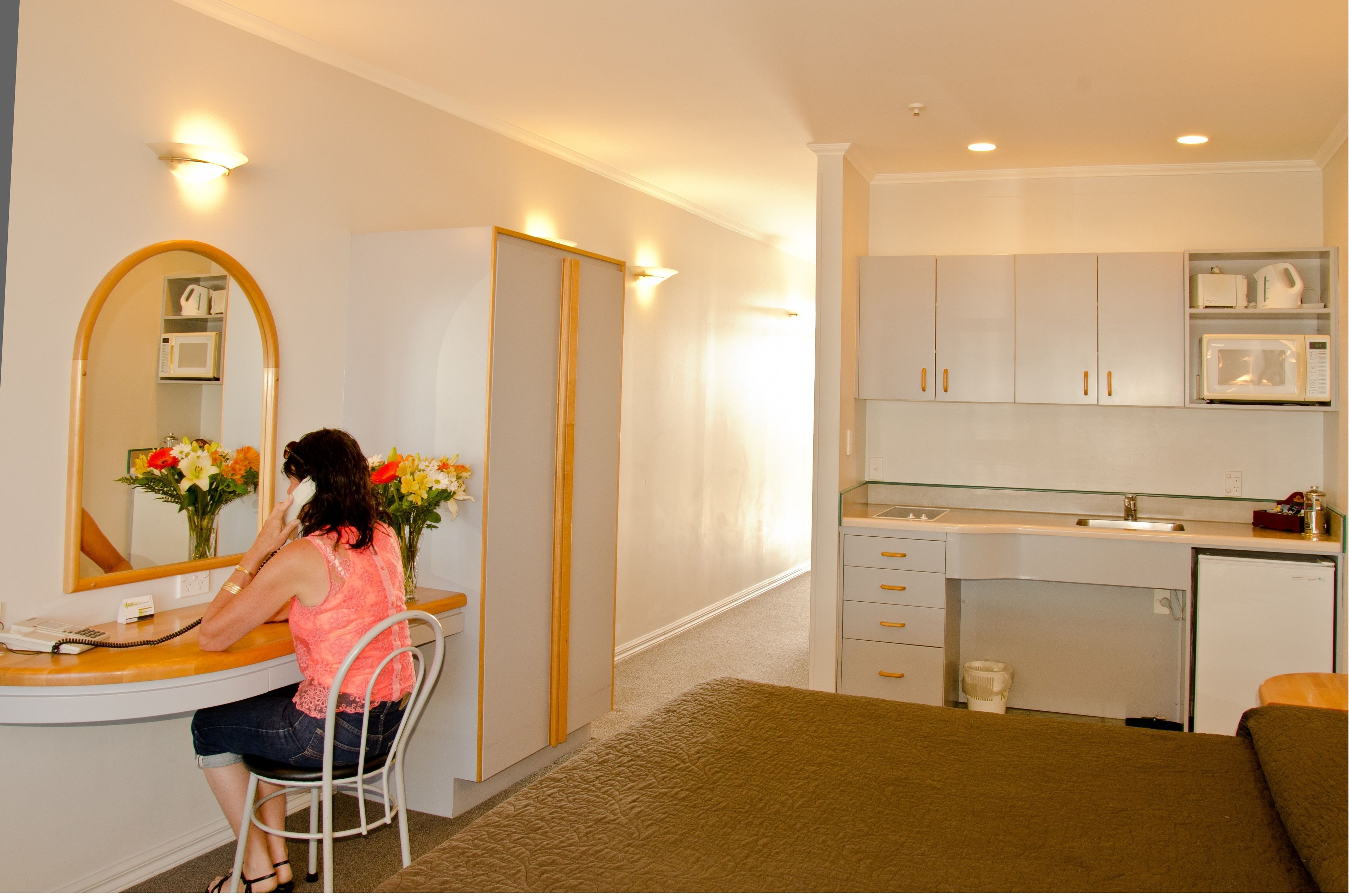 Habitación de hotel compacta con cama, escritorio con teléfono, espejo, kitchenette pequeña con microondas y armario.