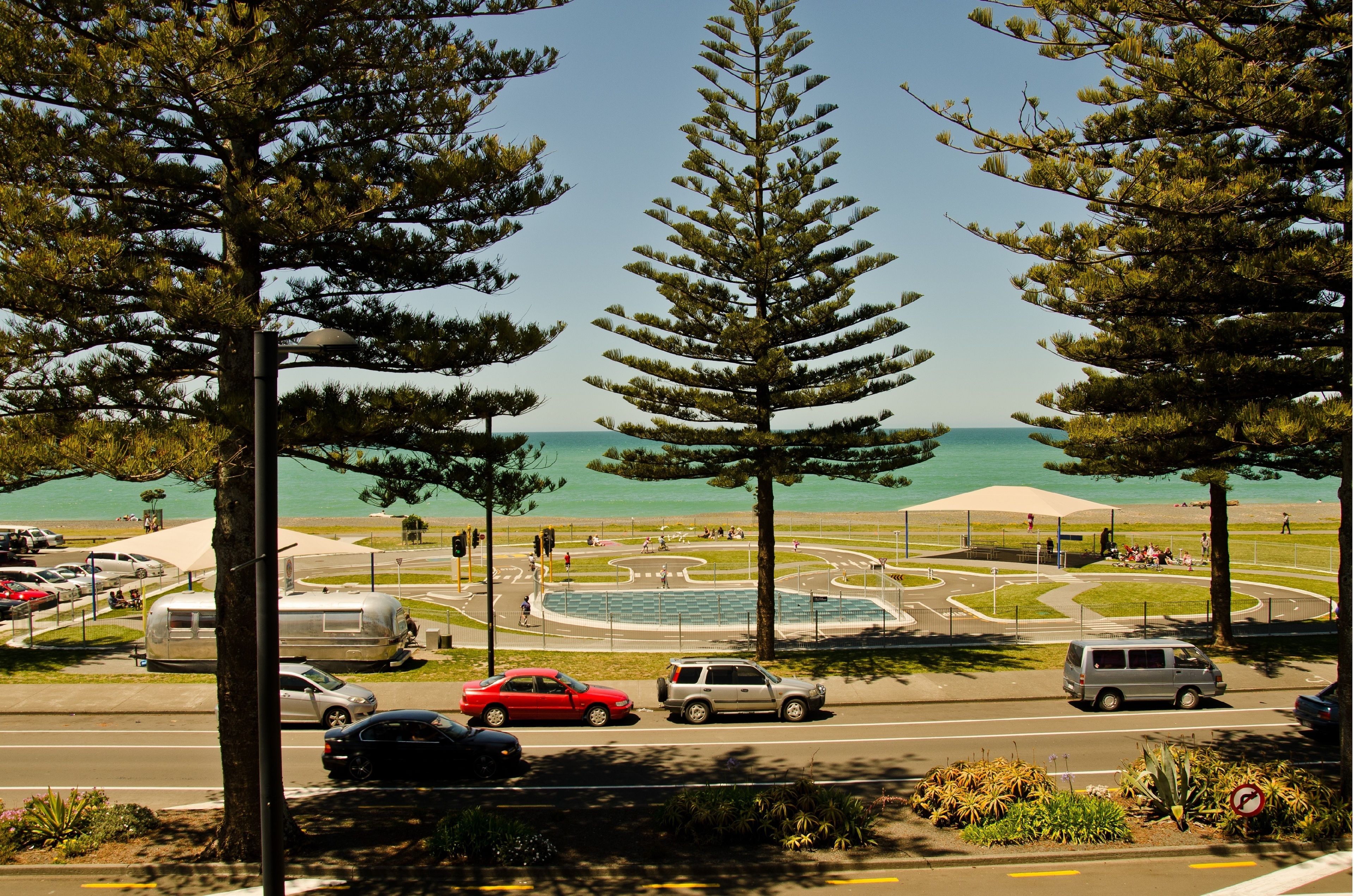 A coastal road with a roundabout, parked cars, and a beach in the background.
