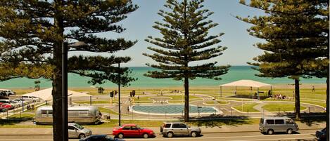 A coastal road with a roundabout, parked cars, and a beach in the background.