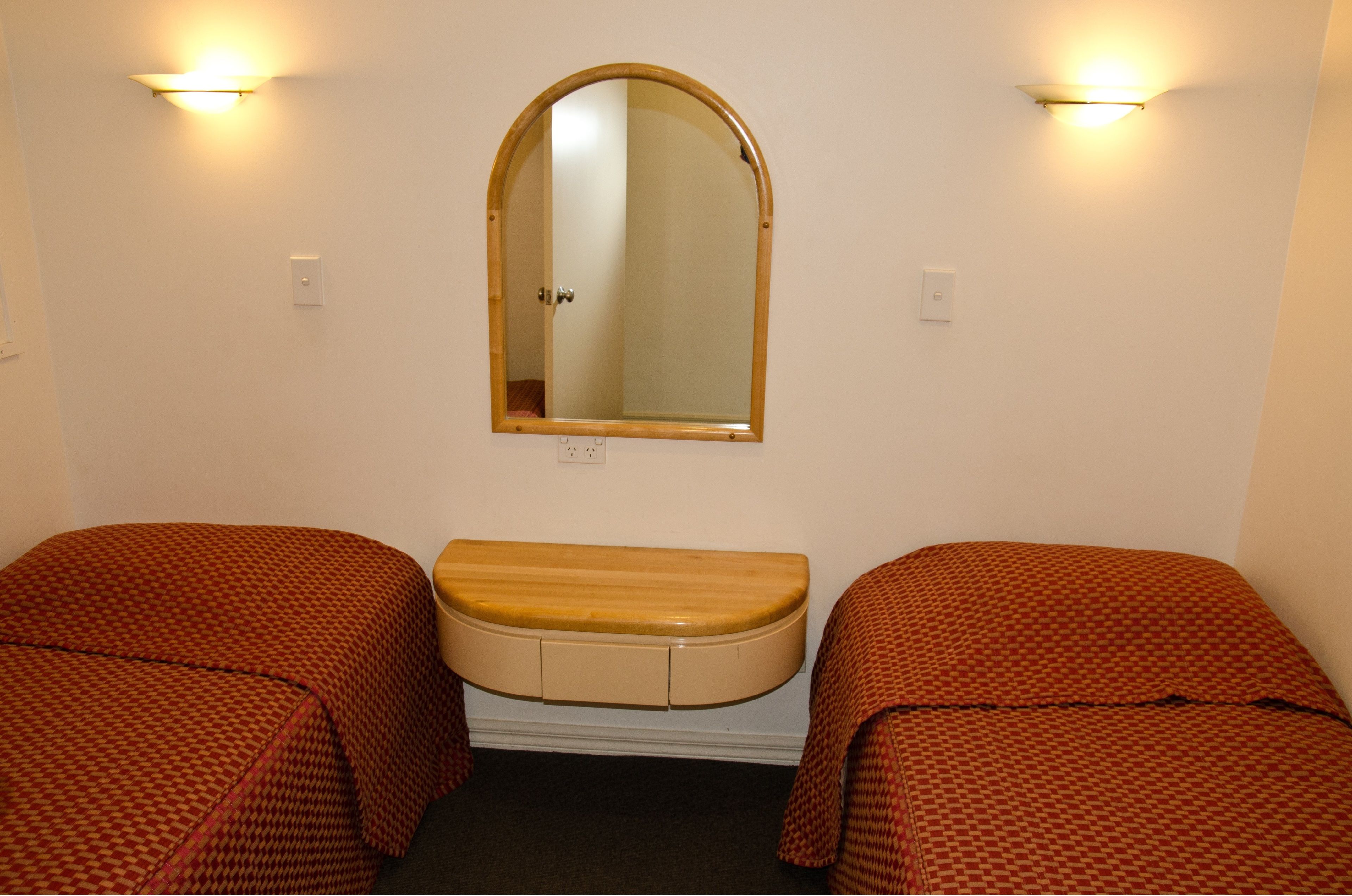A room with two beds, a wooden bench, a mirror, and wall-mounted lights.