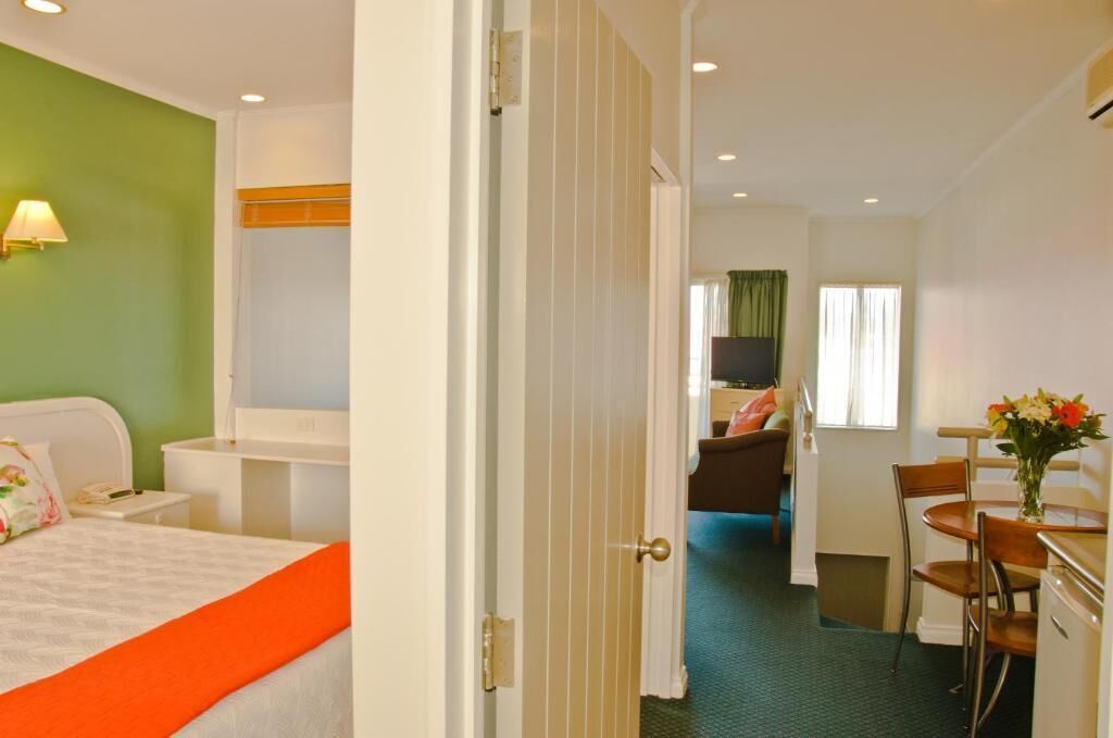 A hotel room with a bed, a desk, a chair, and a dining area.