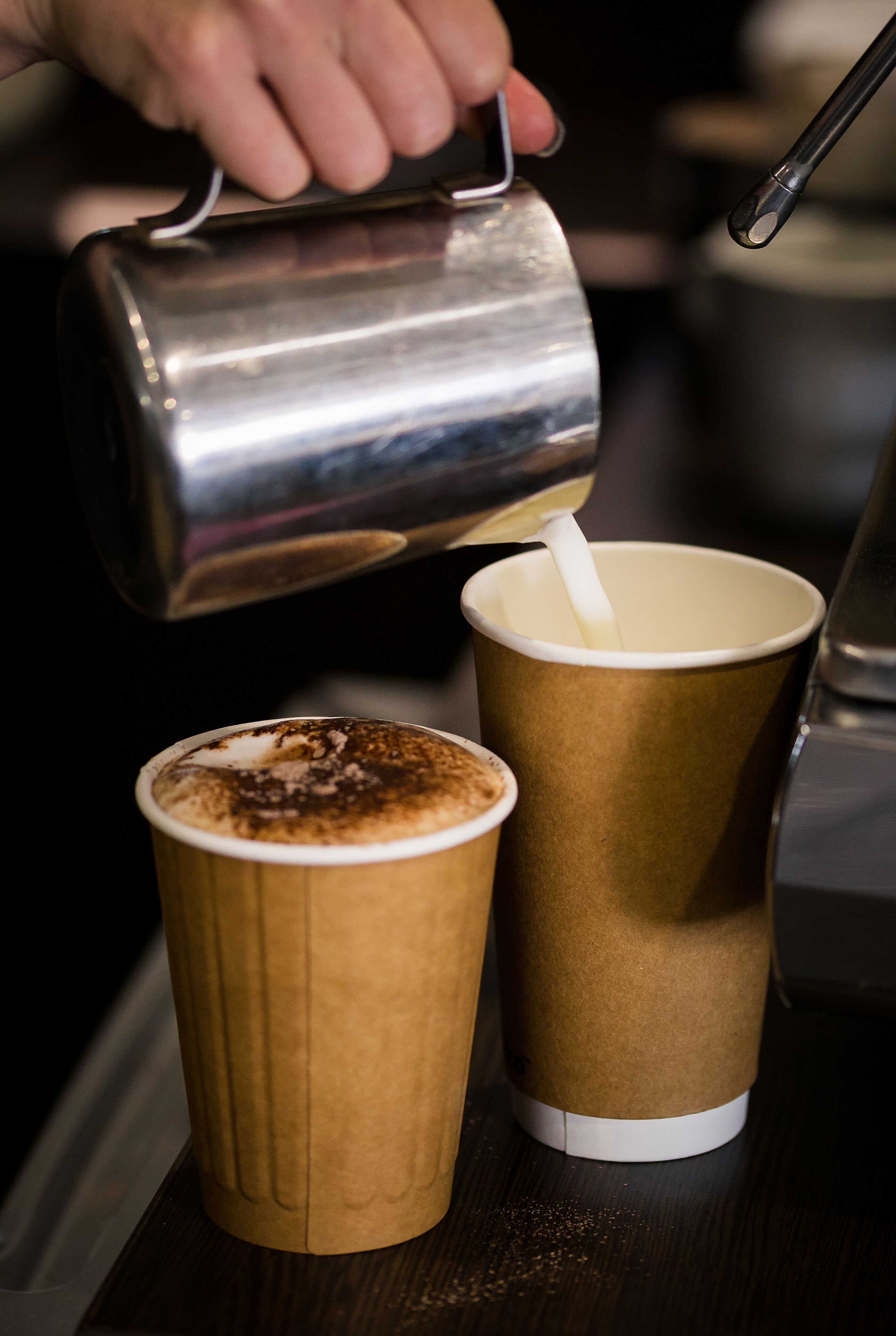 A hand pouring a liquid from a metal container into a paper cup with a straw.