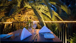 A table set for two with a tropical backdrop, including palm trees and a stone wall.