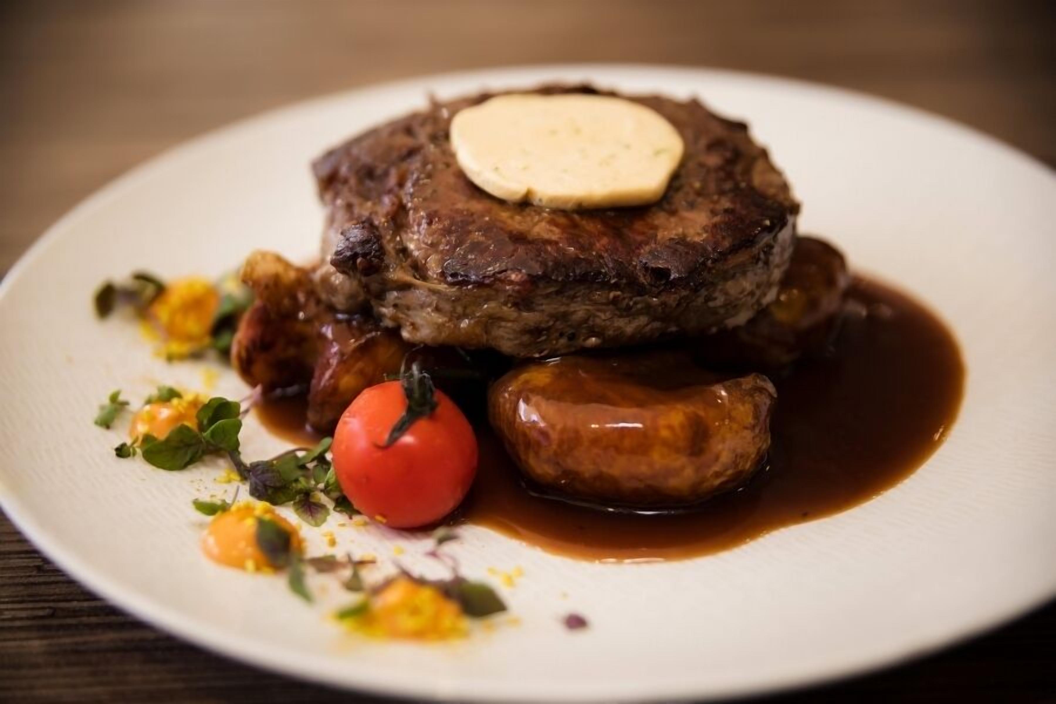 A steak with a pat of butter on top, served with a side of vegetables and sauce.