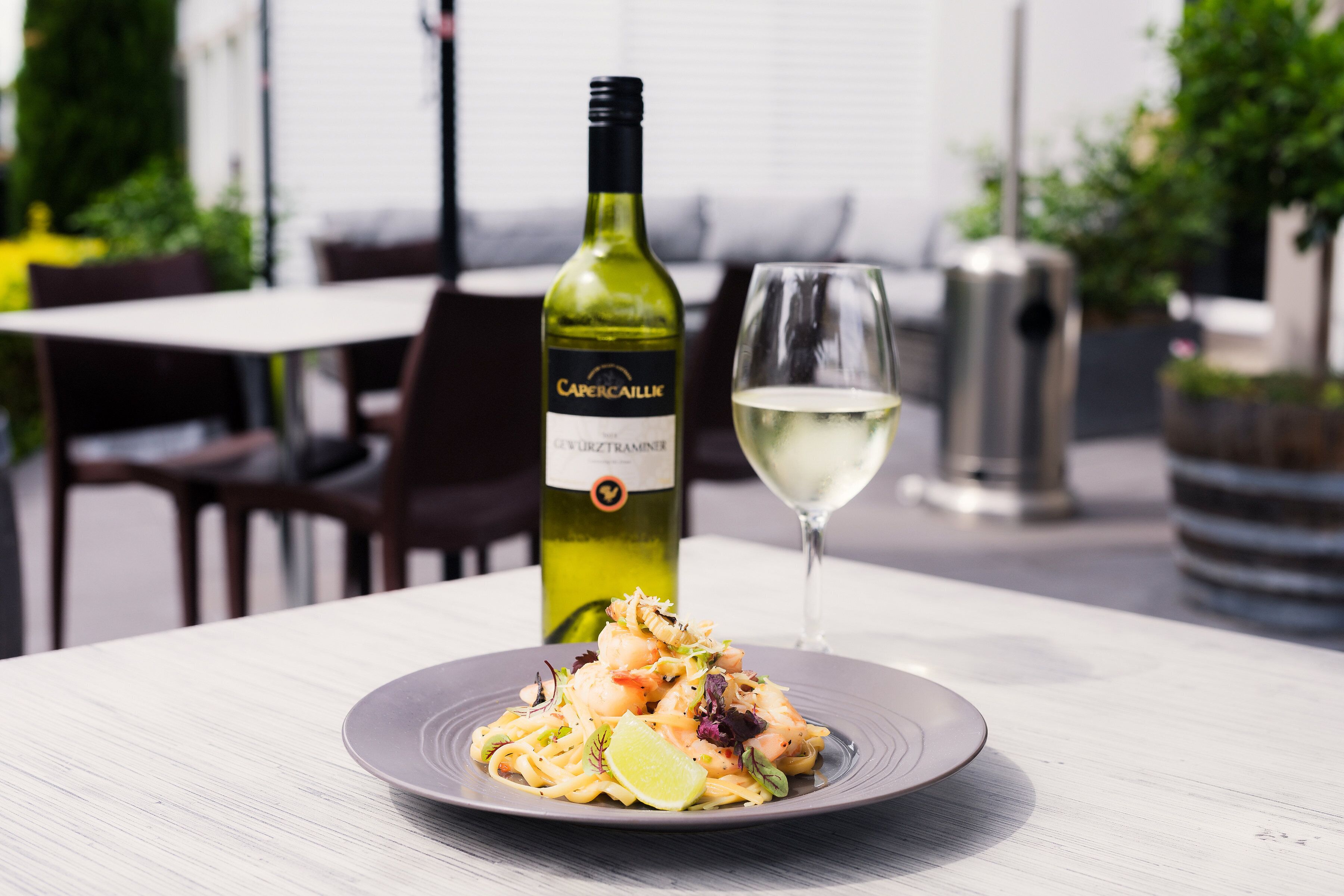 Un tavolo con un piatto di cibo, una bottiglia di vino e un bicchiere di vino bianco.
