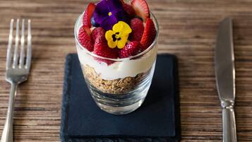 A dessert in a clear glass with strawberries and flowers on top, placed on a dark napkin on a wooden table.
