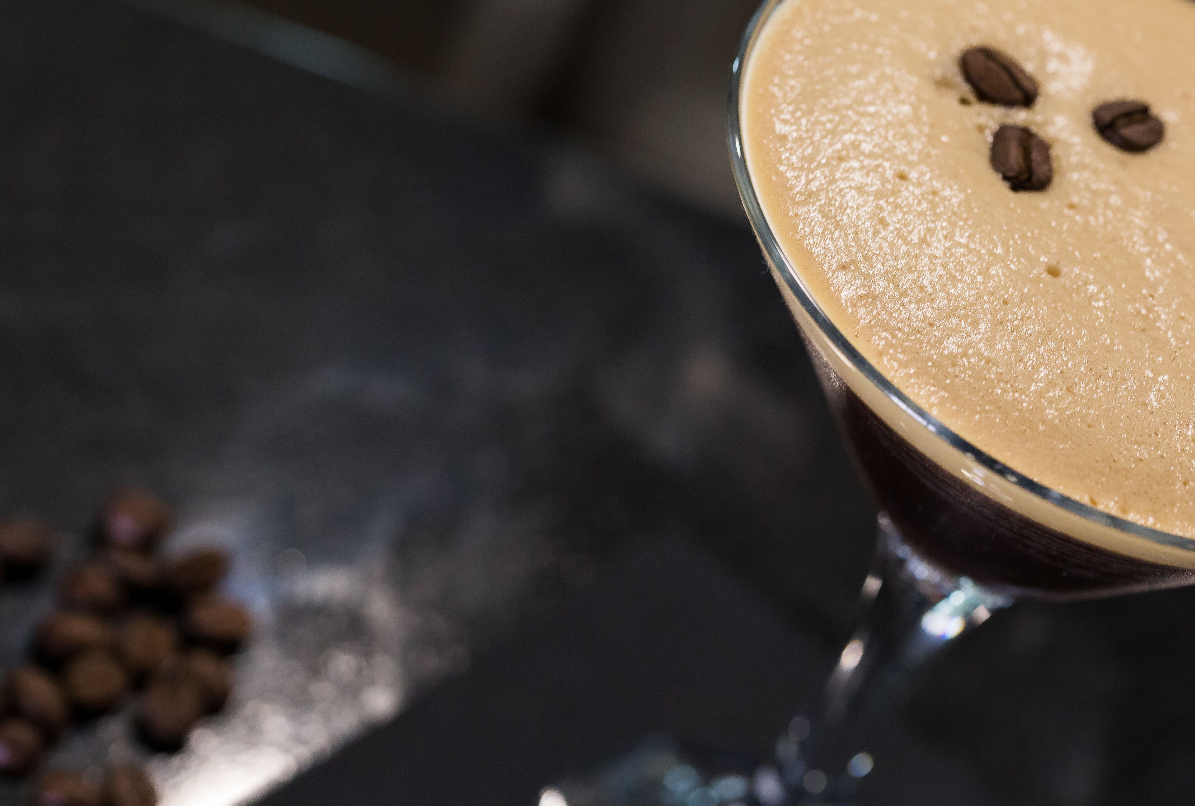 Primer plano de una bebida en un vaso, con una capa cremosa y granos de café encima.