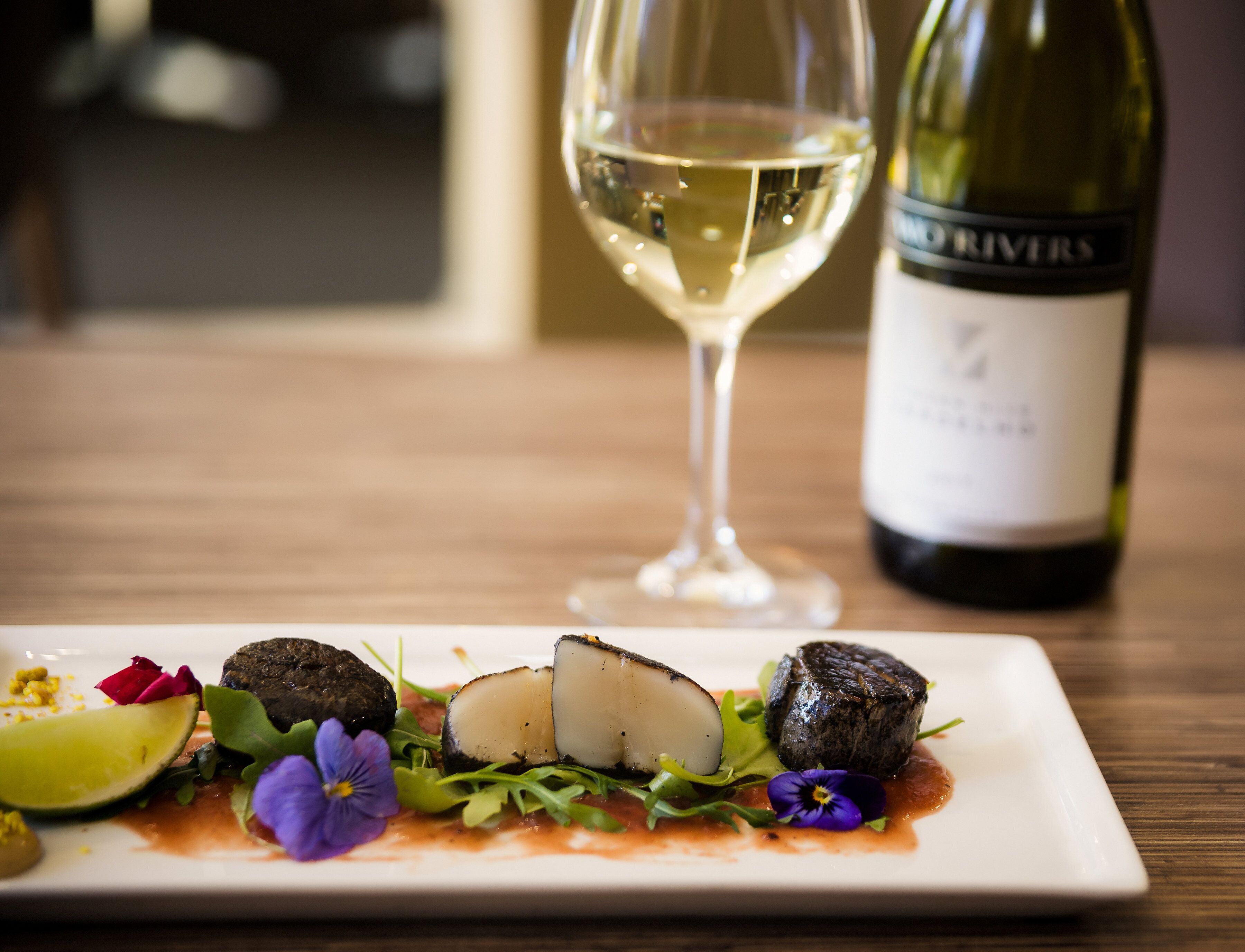 A plate of food with a glass of white wine and a bottle of wine on a wooden table.