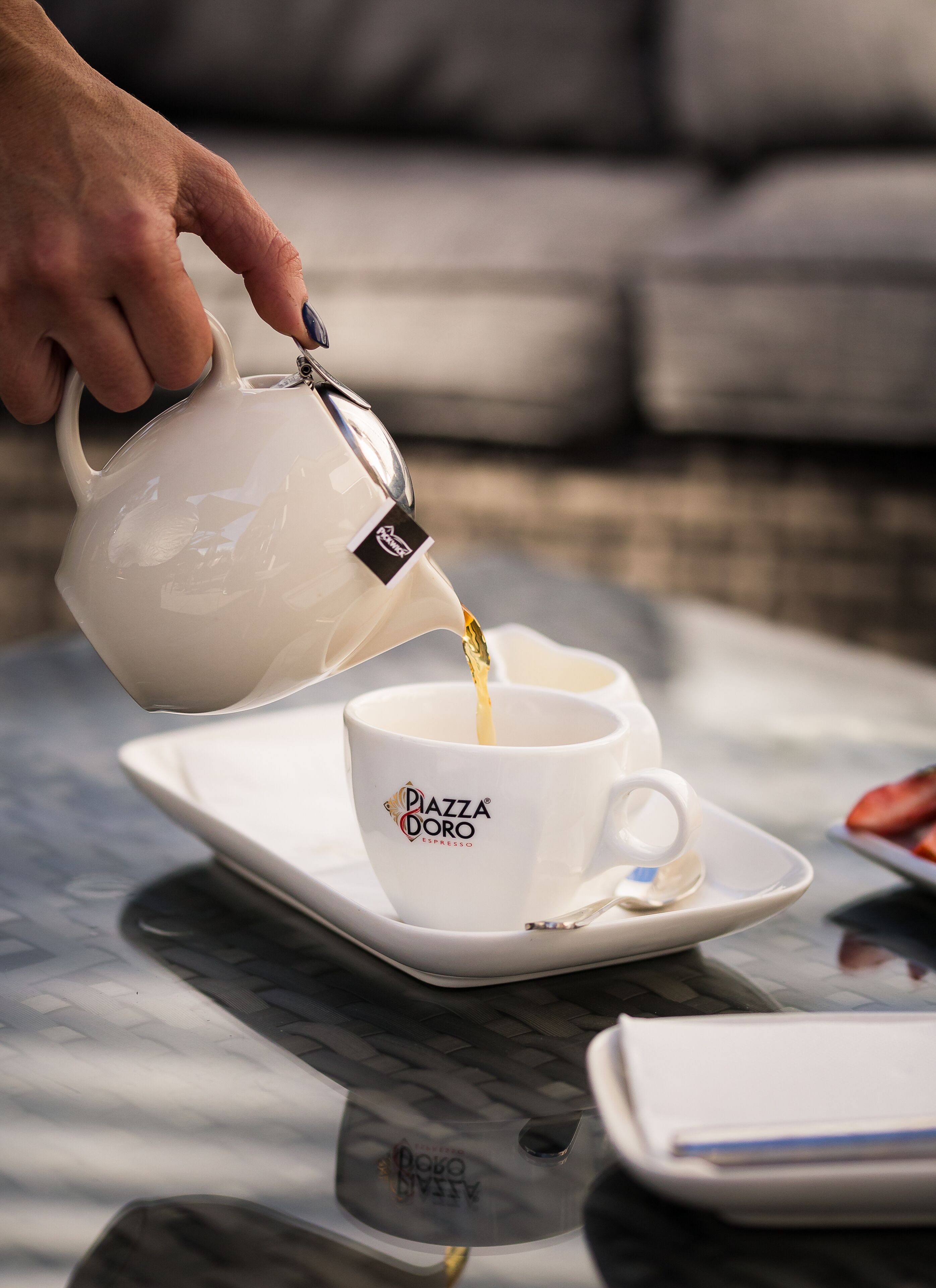 A hand pouring espresso into a white cup with the logo "Piazza Doro Espresso" on a white saucer.