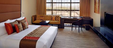 A hotel room with a large bed, a sofa, a desk, and a TV.