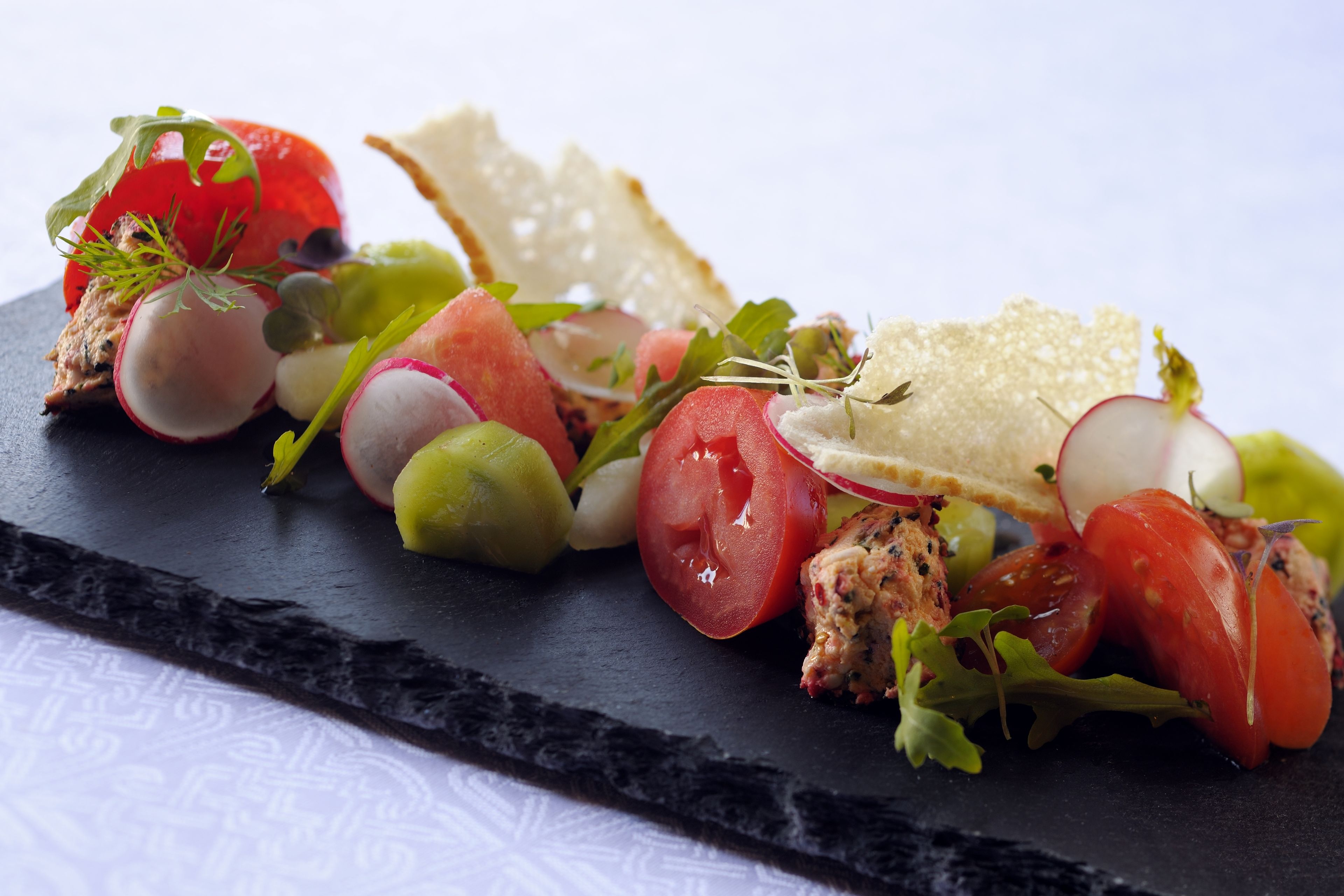 A black slate serving board with a variety of fresh vegetables and a piece of bread.