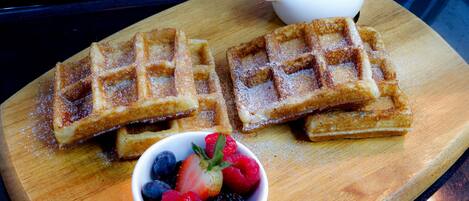 Waffles on a wooden board with a bowl of berries and a small cup of syrup.