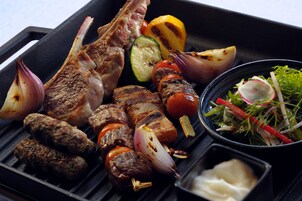 Una parrilla con diversos tipos de carne y verduras, incluyendo chuletas de cordero, brochetas y calabacín a la parrilla.
