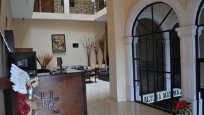 Un hall d’hôtel comprenant un comptoir d’accueil, un espace salon et une grande fenêtre en arc de cercle.