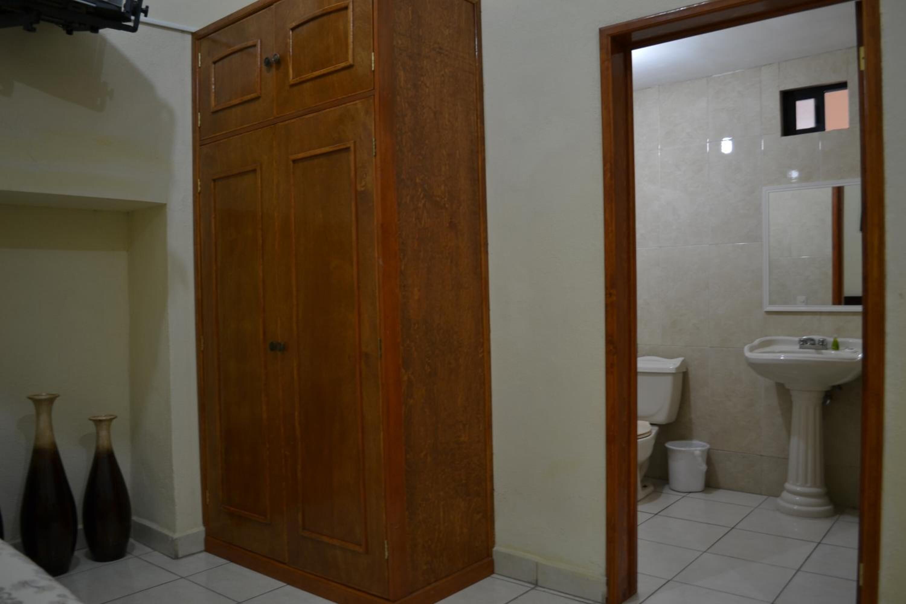 A room with a wooden wardrobe, a white sink, and a toilet.