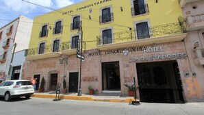Un bâtiment jaune avec une enseigne indiquant « Hôtel Conquistadores » et une voiture noire garée devant.