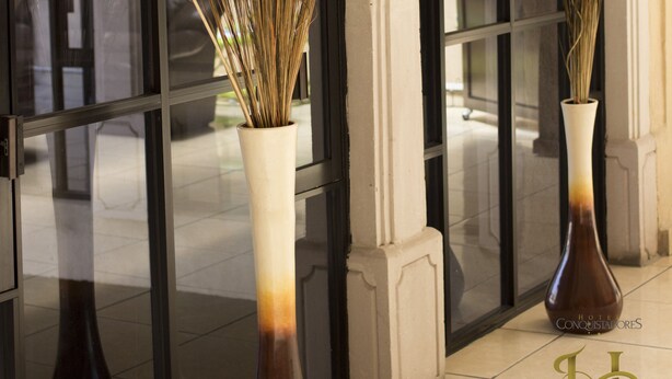 Deux grands vases contenant des plantes séchées sont placés devant une porte en verre dont le cadre est en arc de cercle.