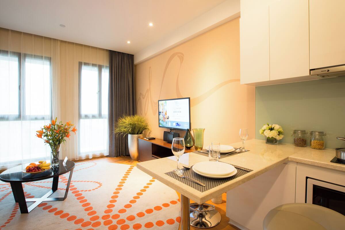 A modern hotel room with a dining area, a television, and a kitchen counter.