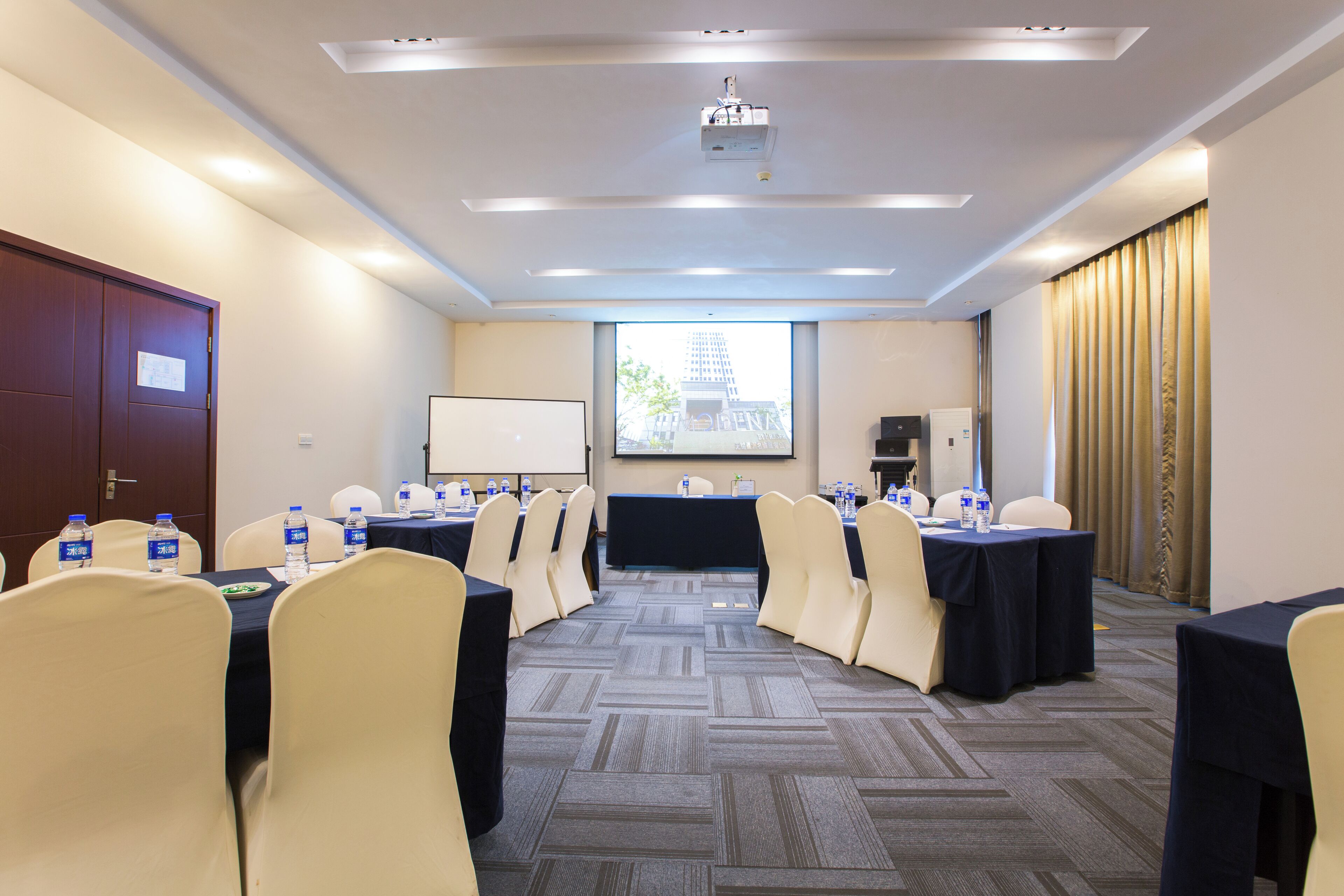Un salón de conferencias con proyector, una pizarra y un amplio ventanal con vista a la ciudad.