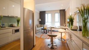 A modern kitchen with a refrigerator, oven, and microwave. There is a dining area with a table and chairs, and a living room with a sofa and a coffee table. - Modena by Fraser New District Wuxi (Wuxi)