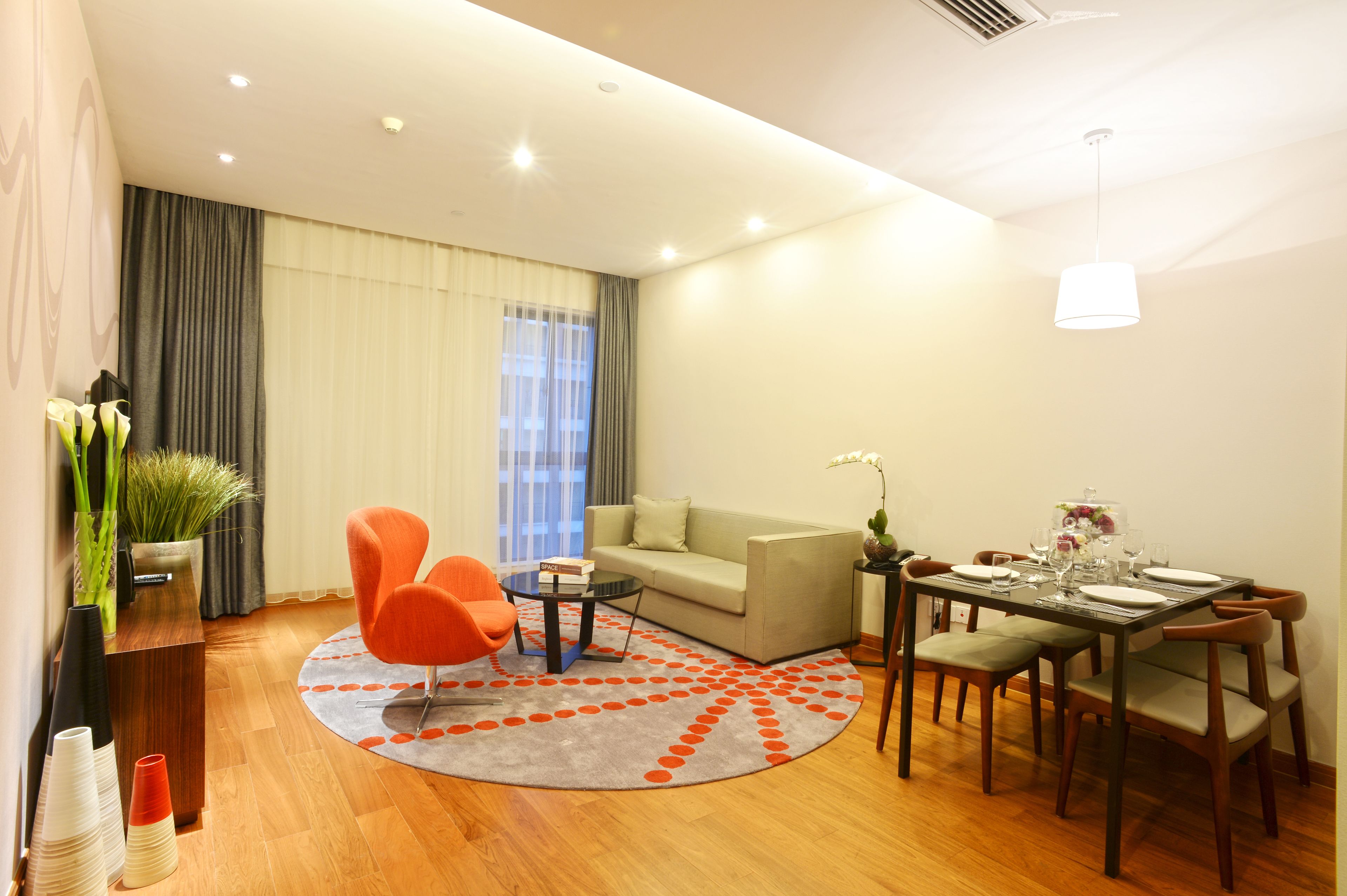 A modern living room with a sofa, orange armchairs, a coffee table, and a dining table set for four.