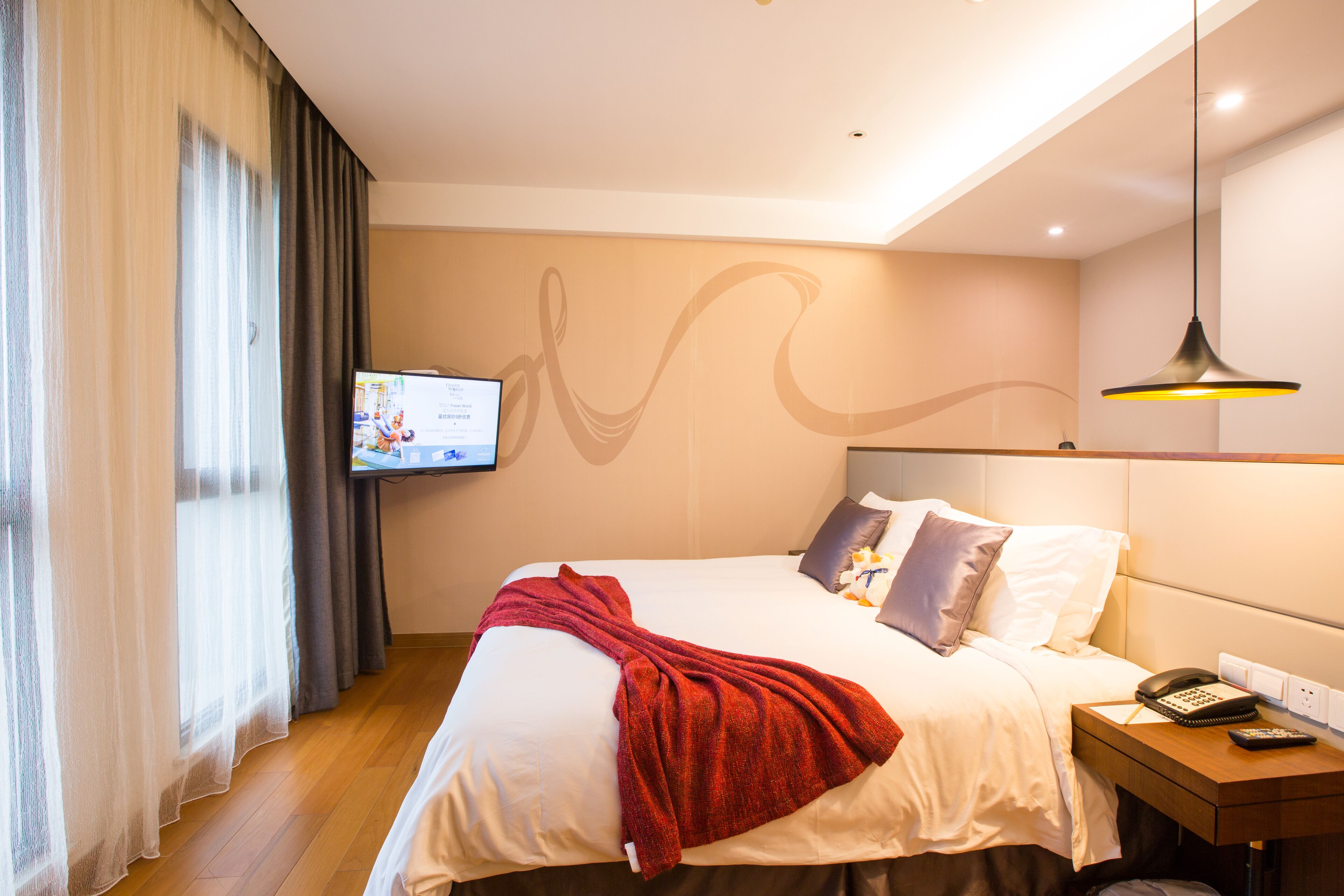 A hotel room with a bed, a TV on the wall, a bedside table with a phone, and a window with curtains.