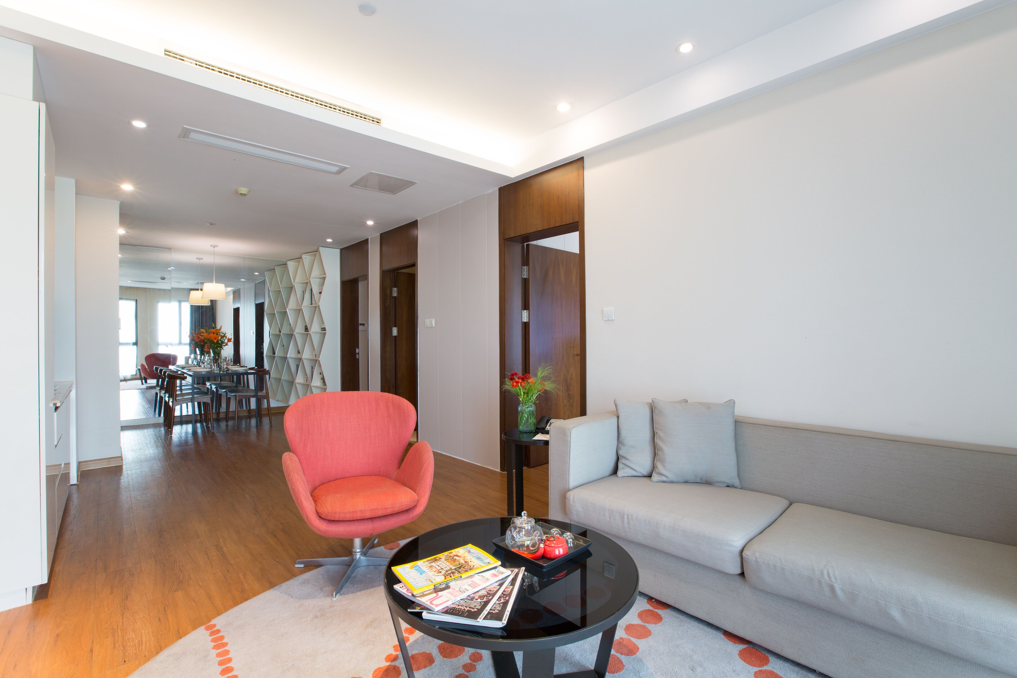 Una sala de estar moderna con un sofá, un sillón rojo, una mesa de centro y un área de comedor al fondo.