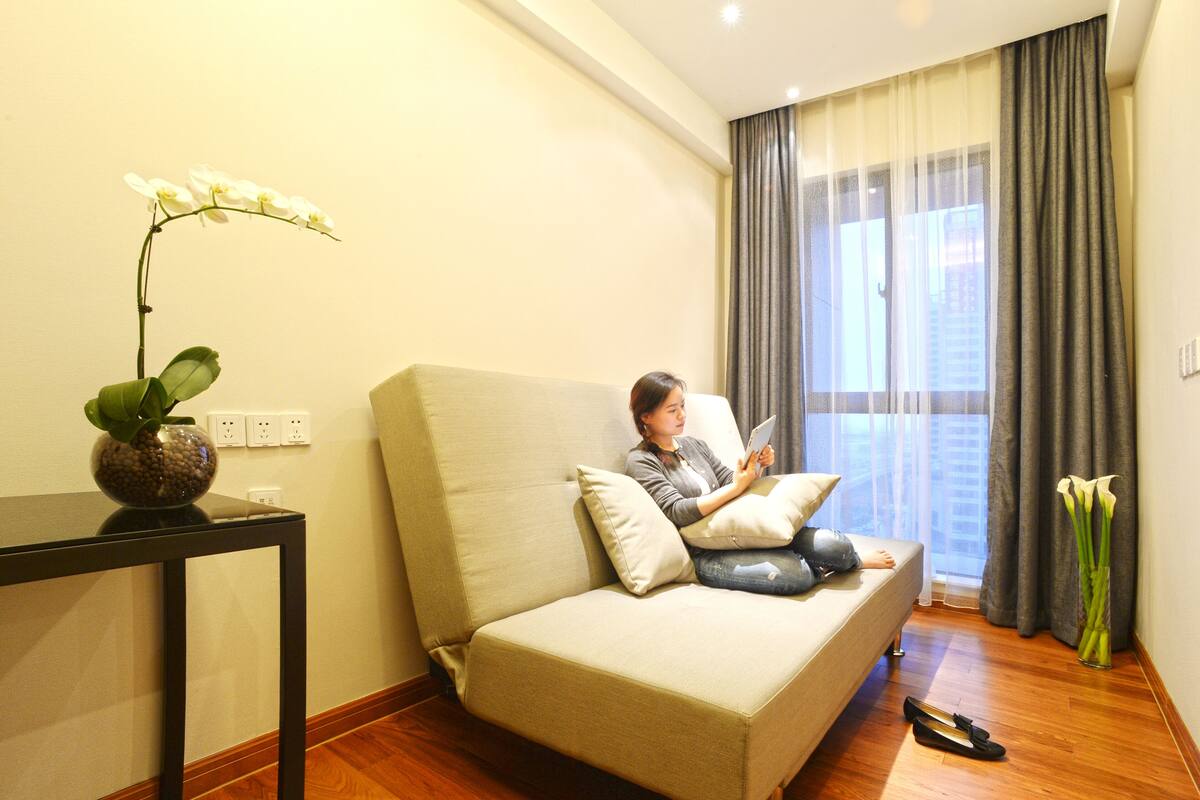 A person sitting on a sofa in a room with a table and a vase of flowers.