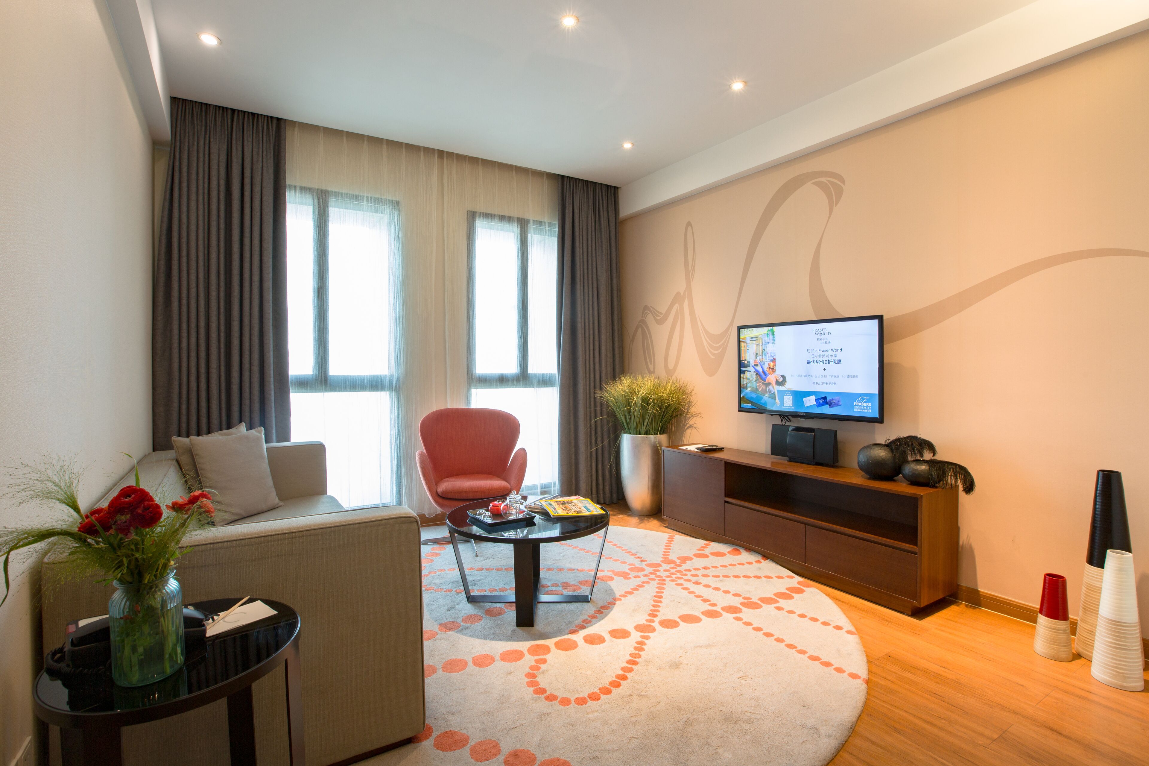 Una sala de estar moderna con un sofá, un sillón rojo, una mesa de centro y un televisor sobre un mueble bajo.